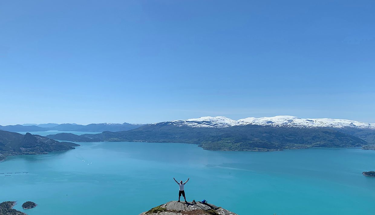 Person on a mountain peak with a view of a turquoise fjord in Hardanger.