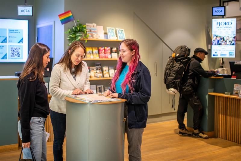 Ansatt som hjelper to kunder i turistinformasjonen