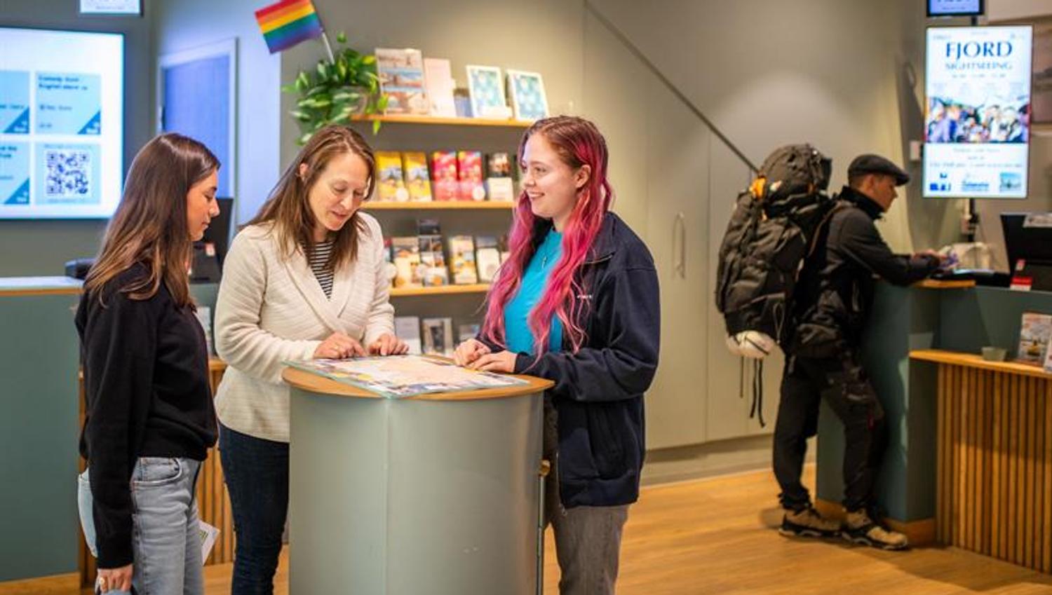 Ansatt som hjelper to kunder i turistinformasjonen
