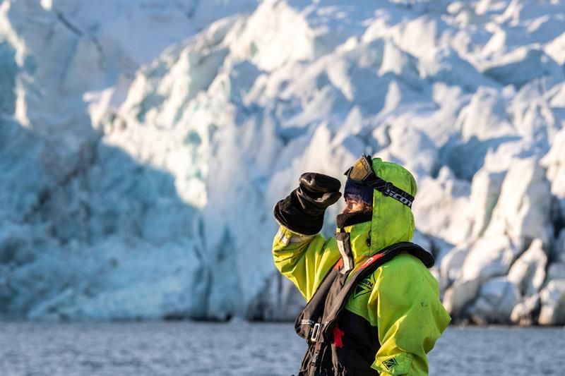 Person speider ut fjorden isbre foran blå isvegg.