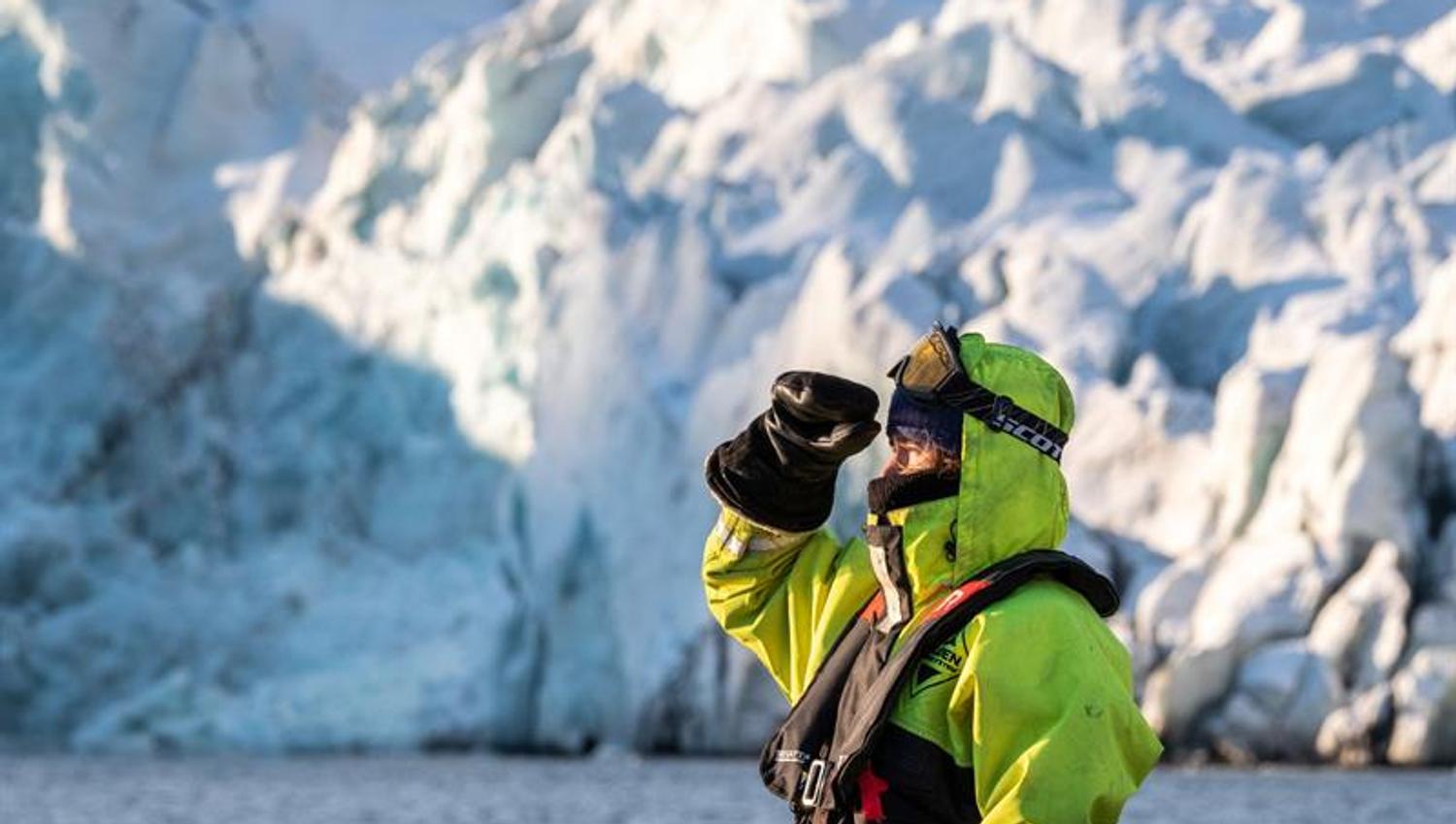 Person speider ut fjorden isbre foran blå isvegg.