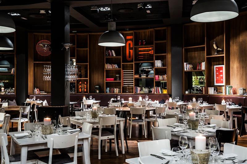 Restaurant interior: Small white tables and chairs, large bookshelves and gray ceiling lights.