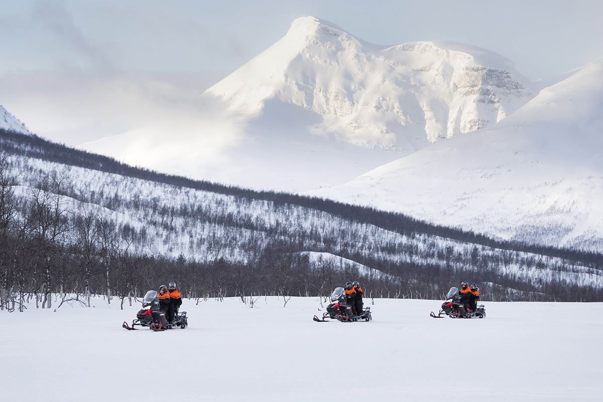 Three snow scooters drive past massive mountains