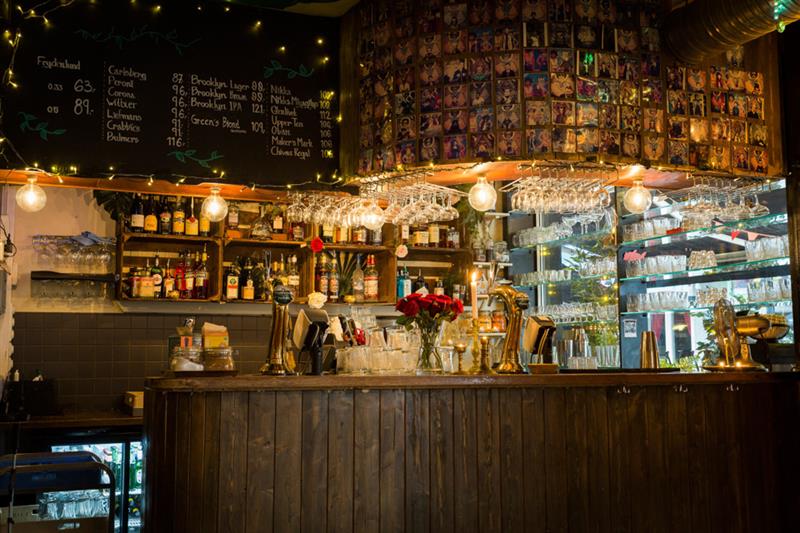 Interior of bar area med glasses, bottles, beer tap and a blackboard.