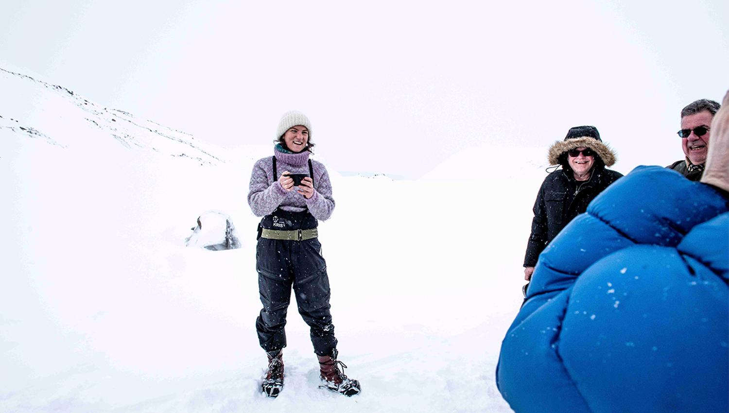 A guide holding a cup with hot drink in it while talking to guests in snowy surroundings on a glacier