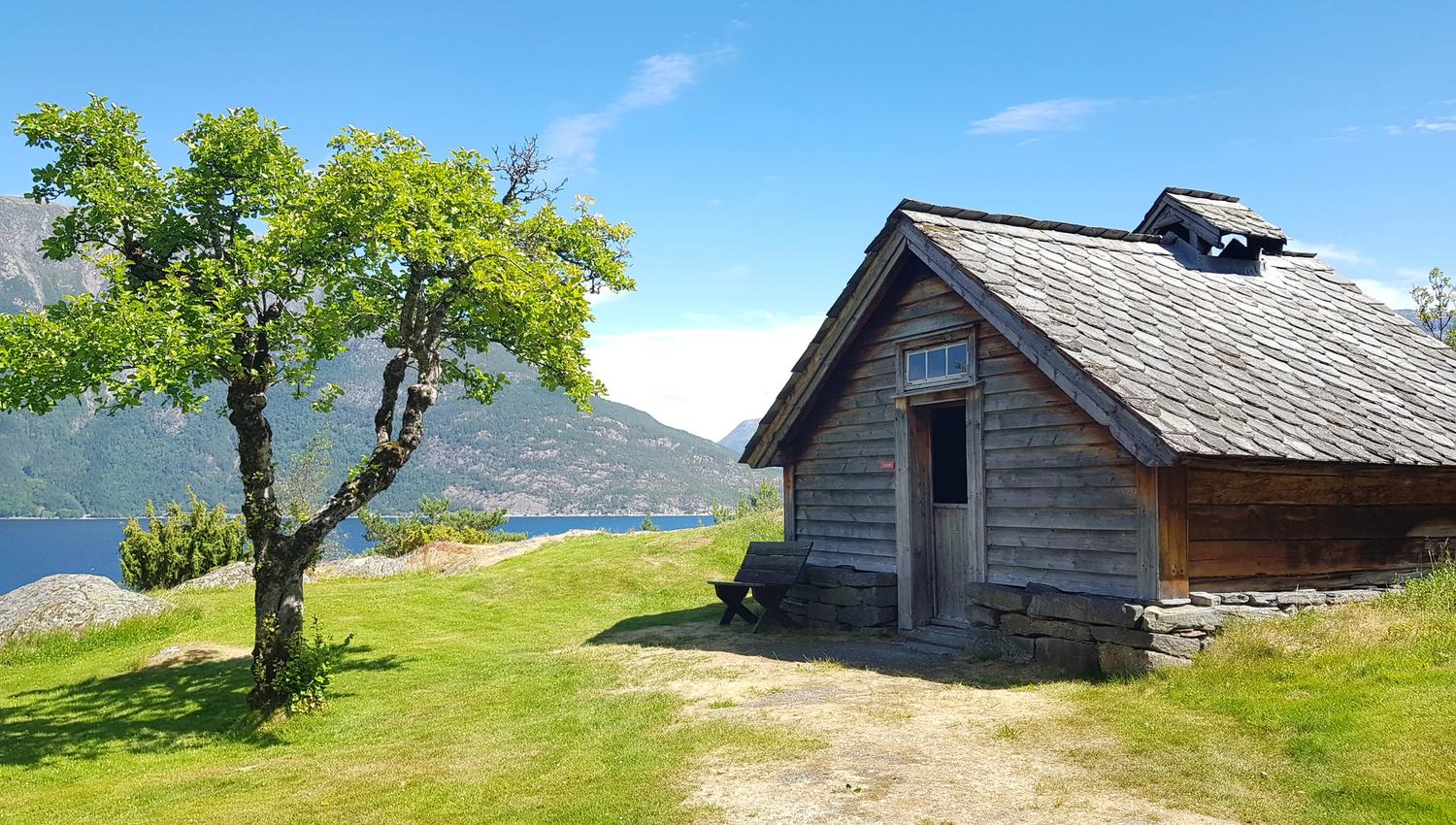 Gamal tømrahytte i friluftsmuseet med utsikt over fjord og fjell i Hardanger.
