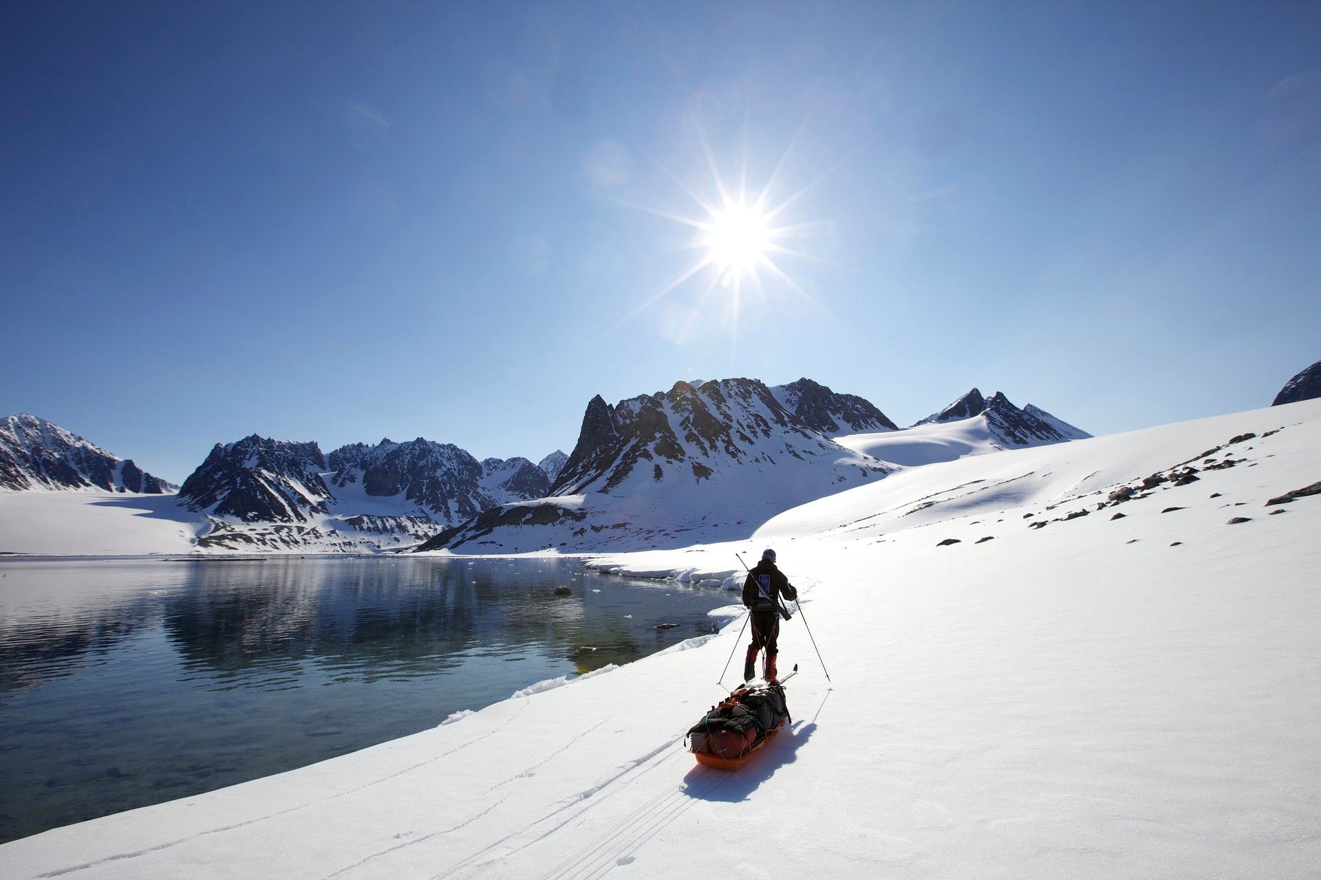 A person skiing and pulling a sled along a shoreline