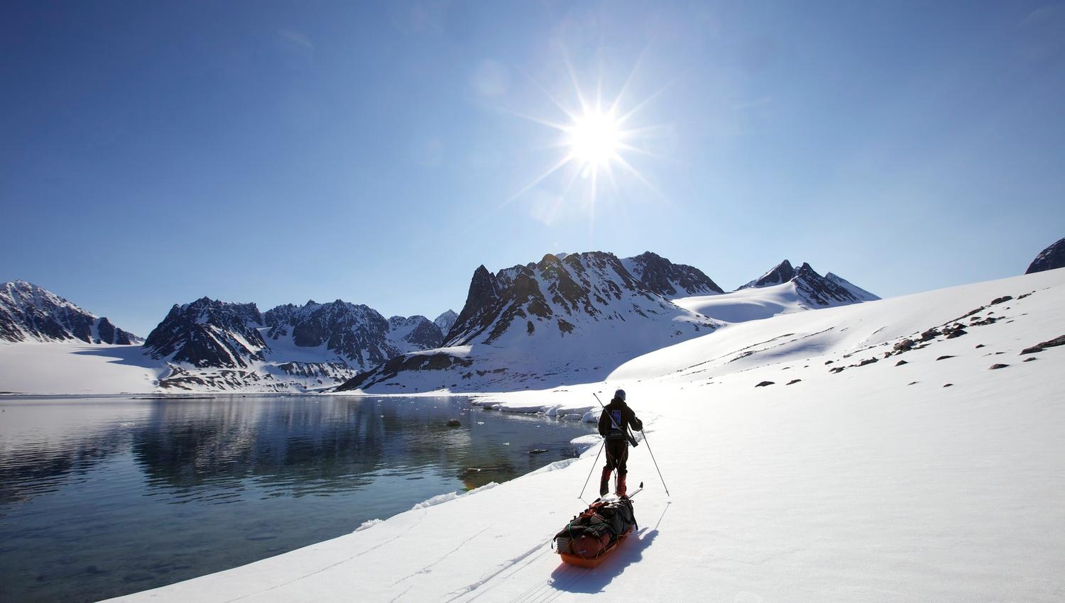 A person skiing and pulling a sled along a shoreline