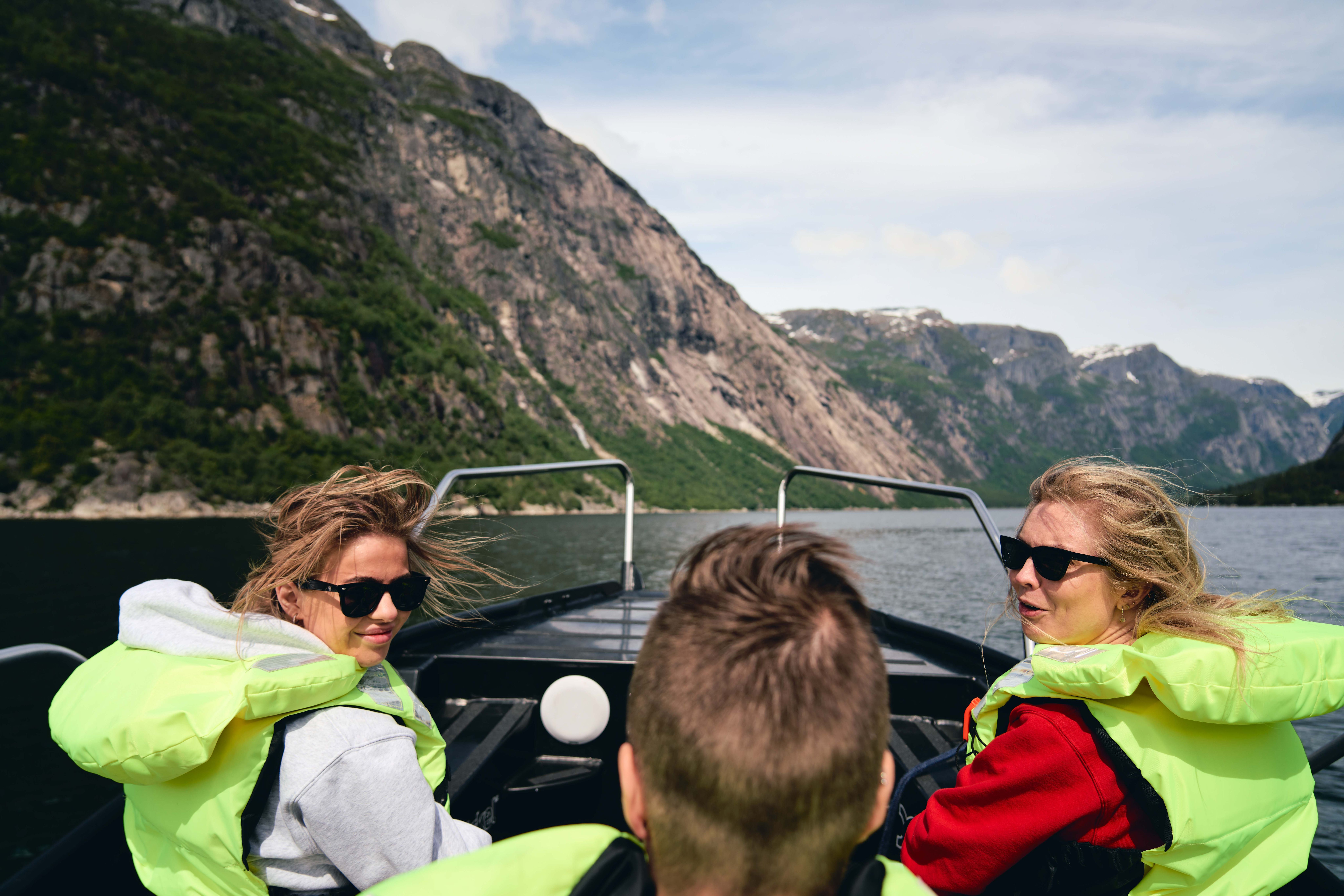 Tre passasjerer med vind i håret ler ombord i båten.