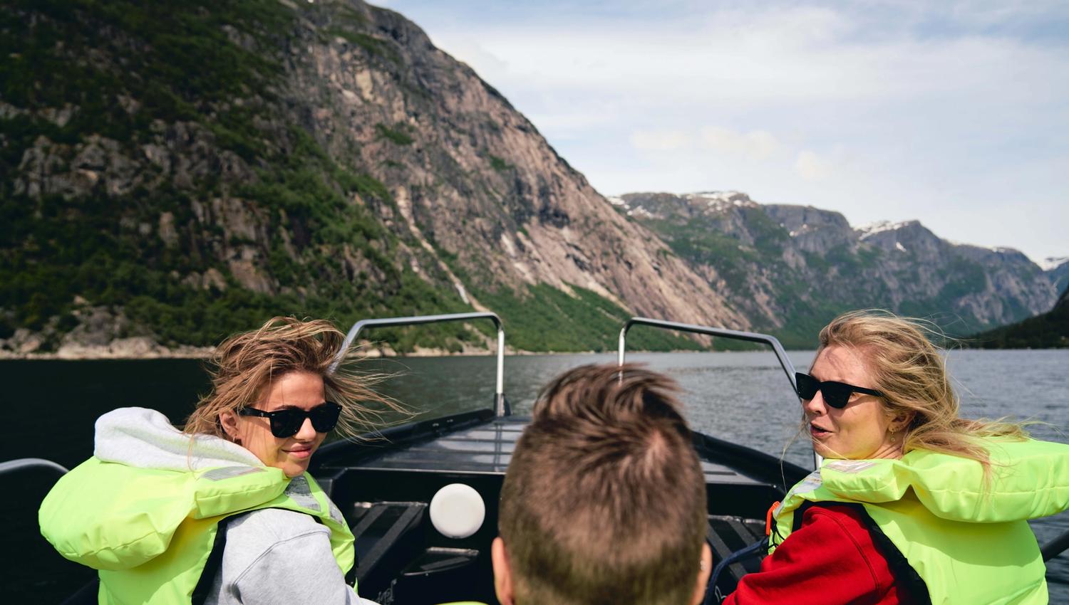 Tre passasjerer med vind i håret ler ombord i båten.
