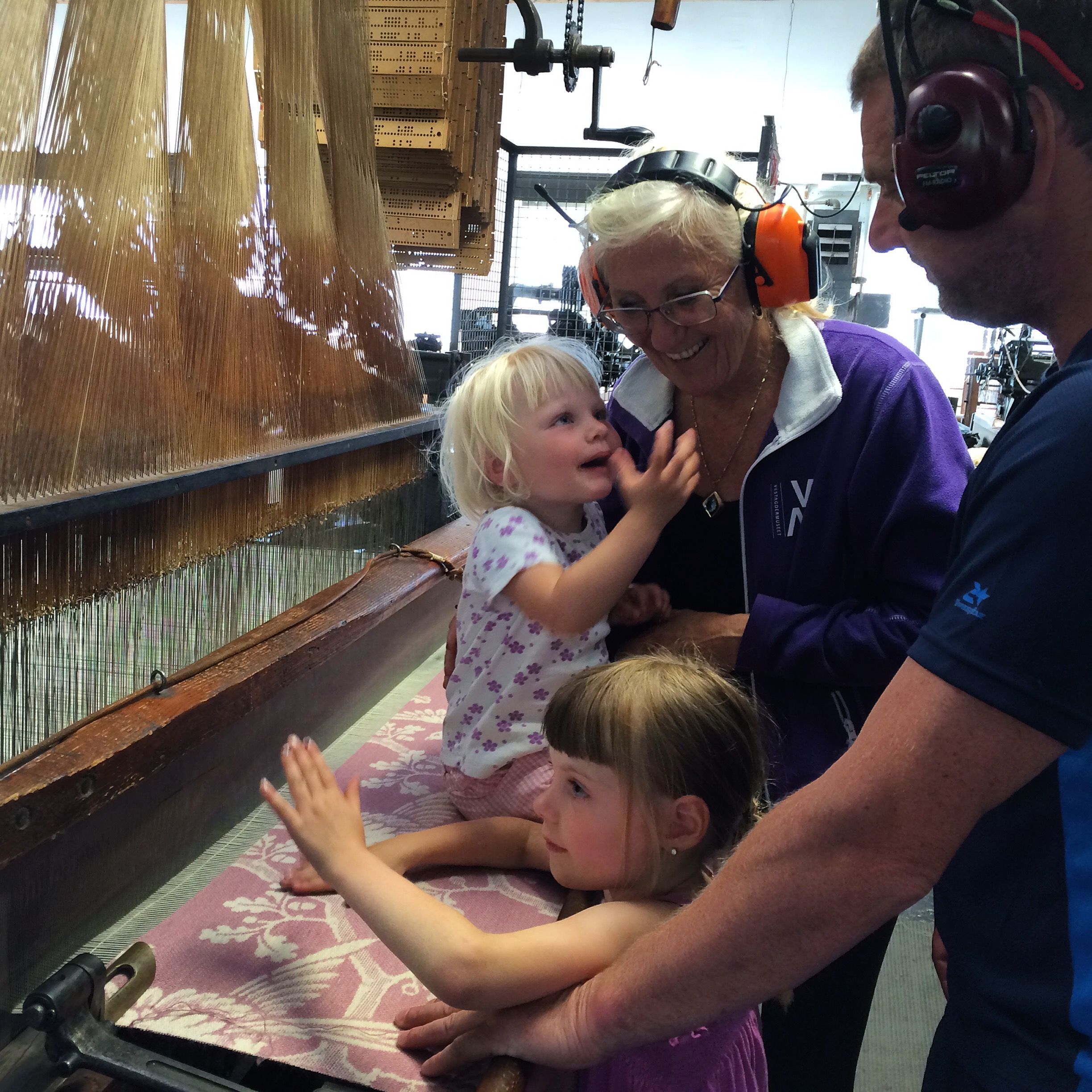 Two children and two adults feeling and touching the weaving machine.