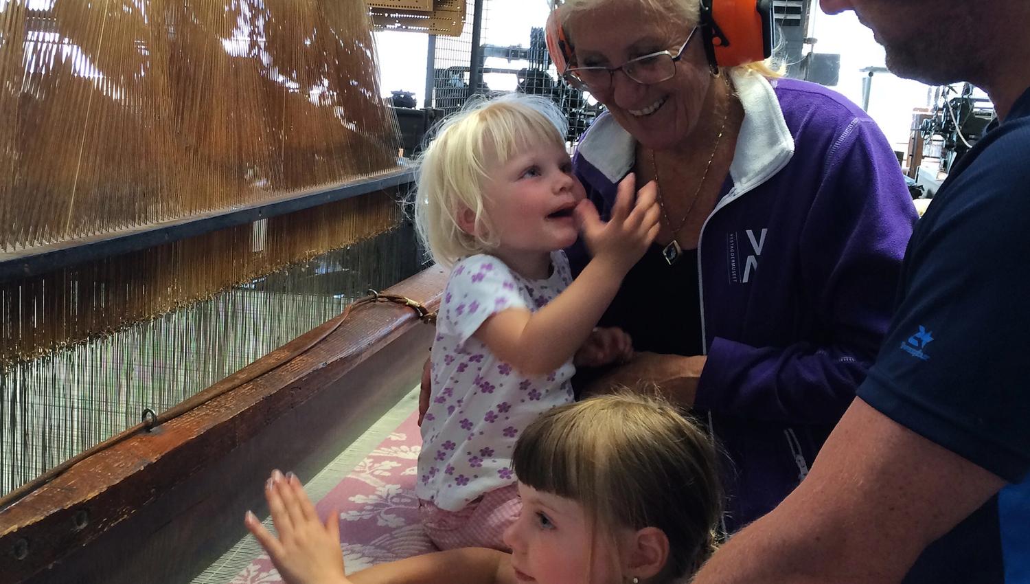 Two children and two adults feeling and touching the weaving machine.