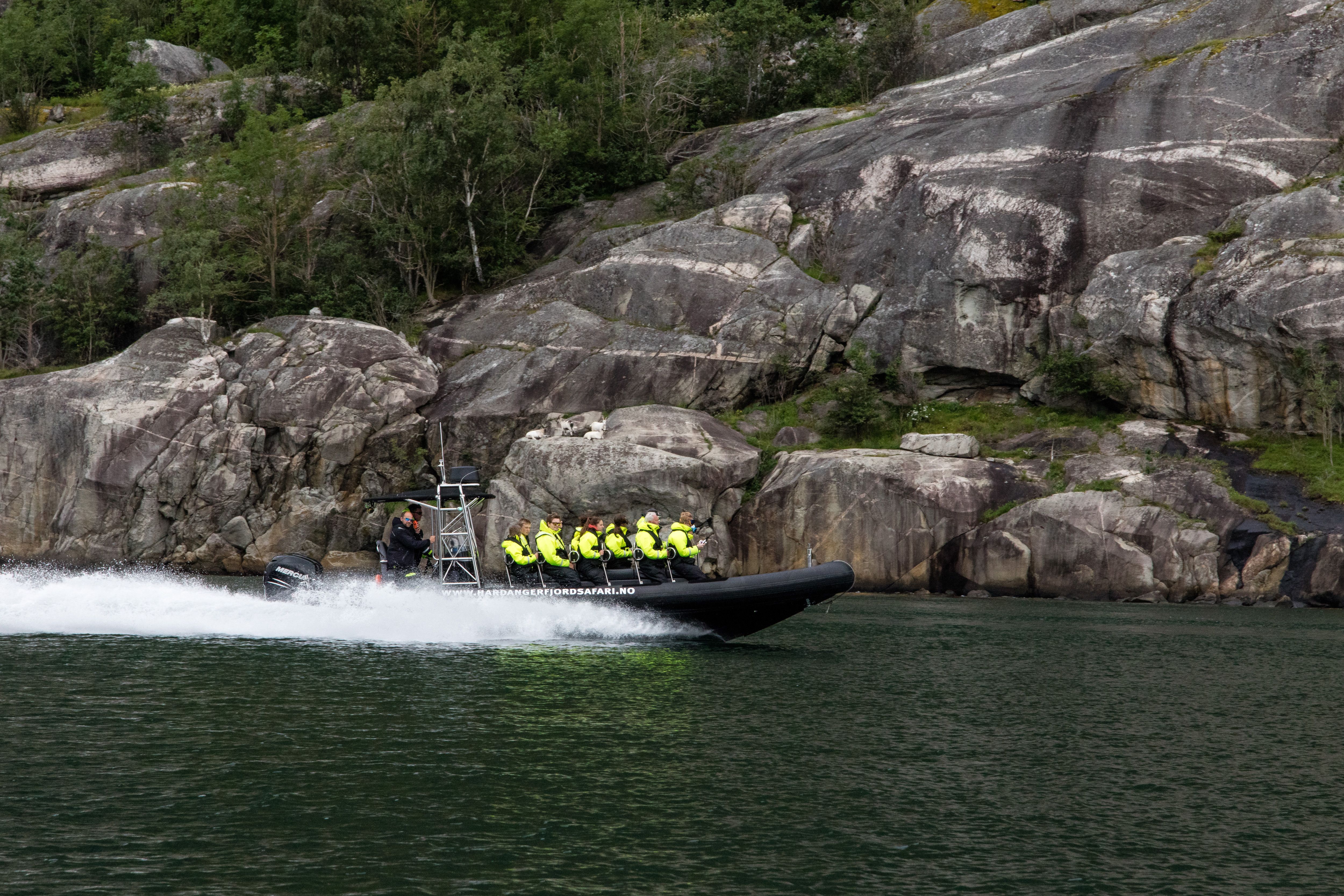 En ribbåt fylt med passasjerer i fart langs fjorden.