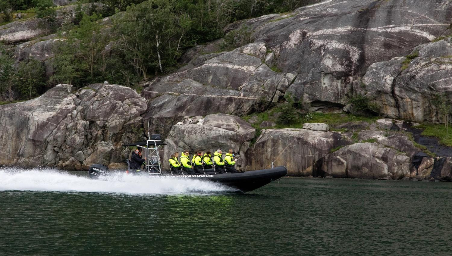 En ribbåt fylt med passasjerer i fart langs fjorden.