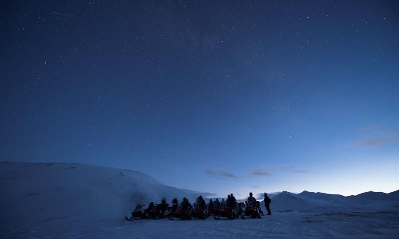 Dark blue nightsky with people and snowmobiles on the ground.