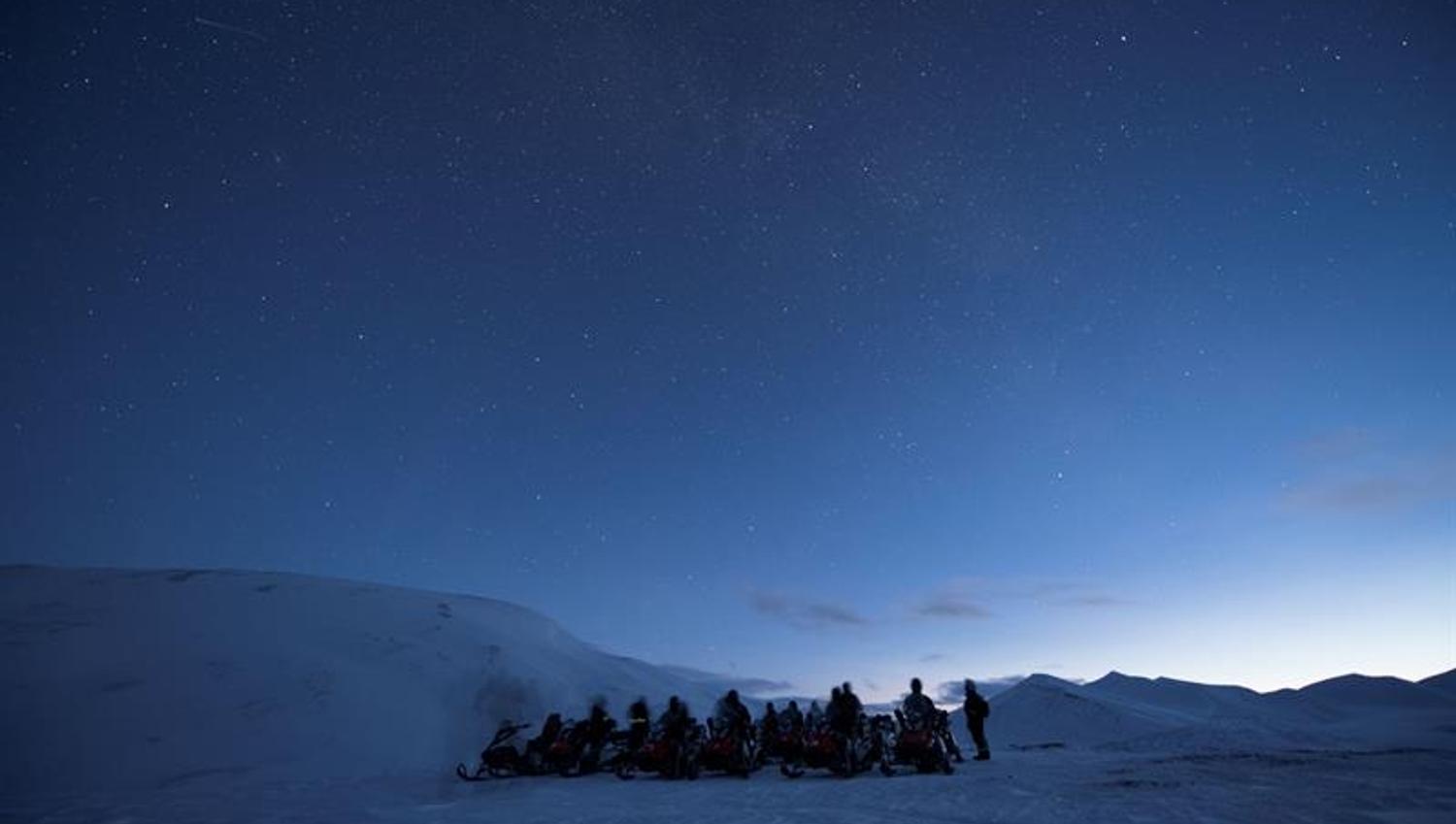 Dark blue nightsky with people and snowmobiles on the ground.