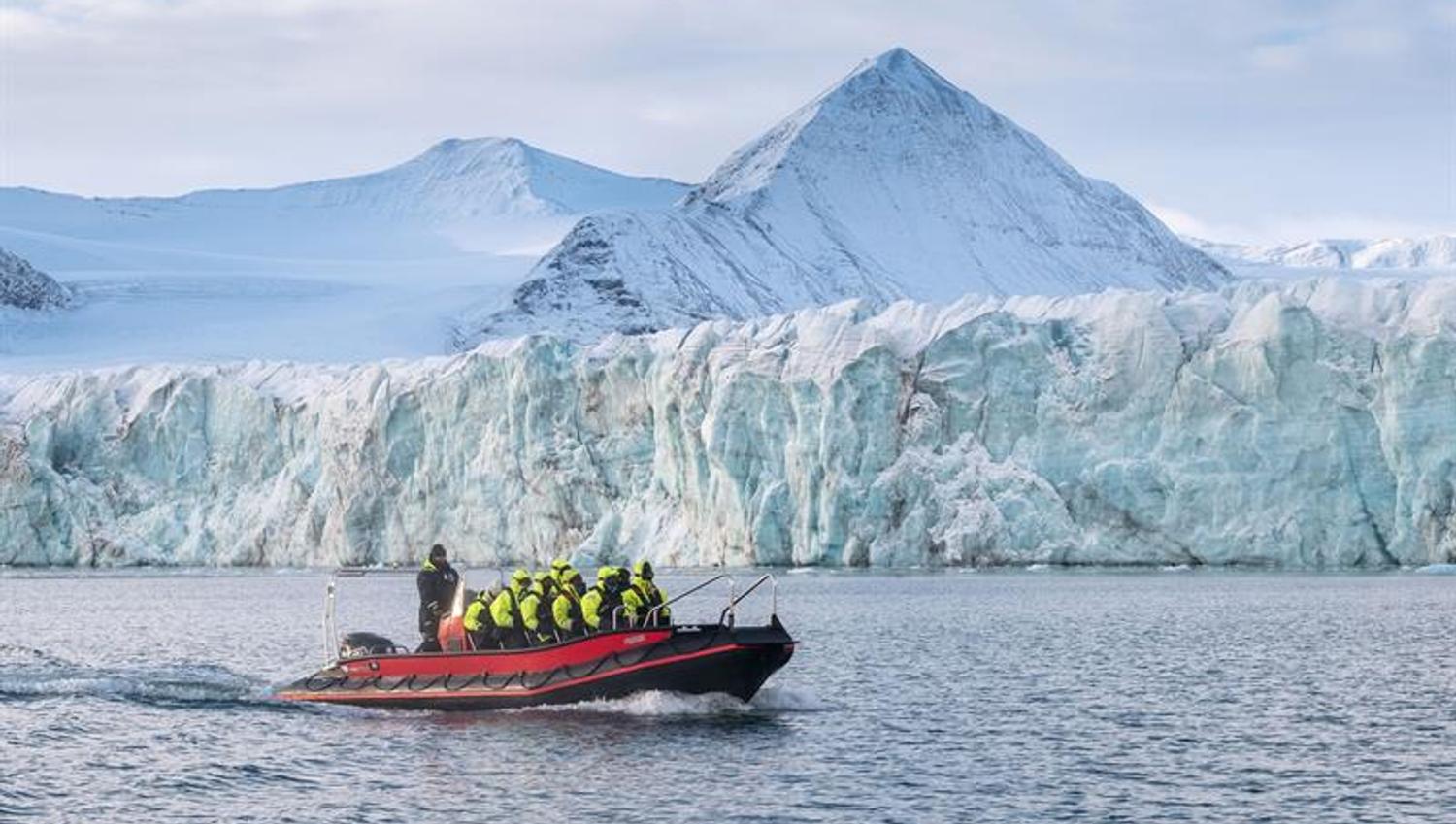 Båt kjører på fjorden med isbre og fjell i bakgrunnen