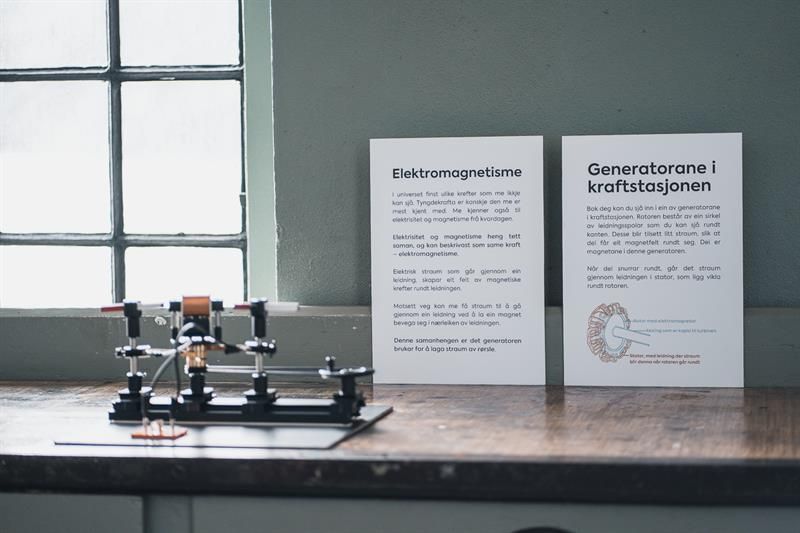 Informasjonstavle om elektromagnetisme og generatorar på Kraftmuseet, med utstilling av ein liten modell.