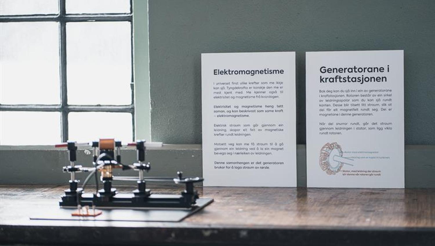 Informasjonstavle om elektromagnetisme og generatorar på Kraftmuseet, med utstilling av ein liten modell.
