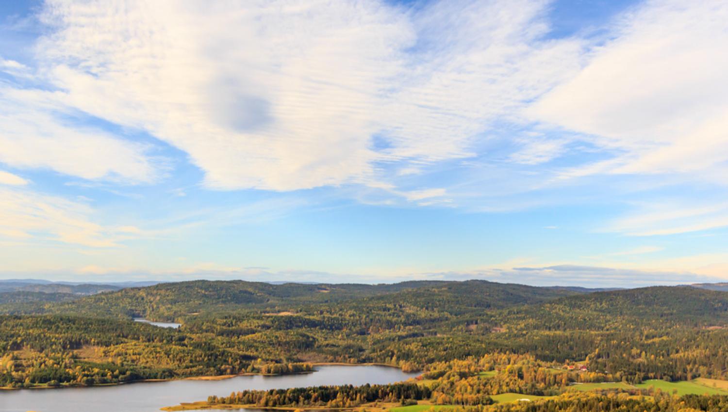 Blå himmel med skyer over idyllisk naturlandskap.