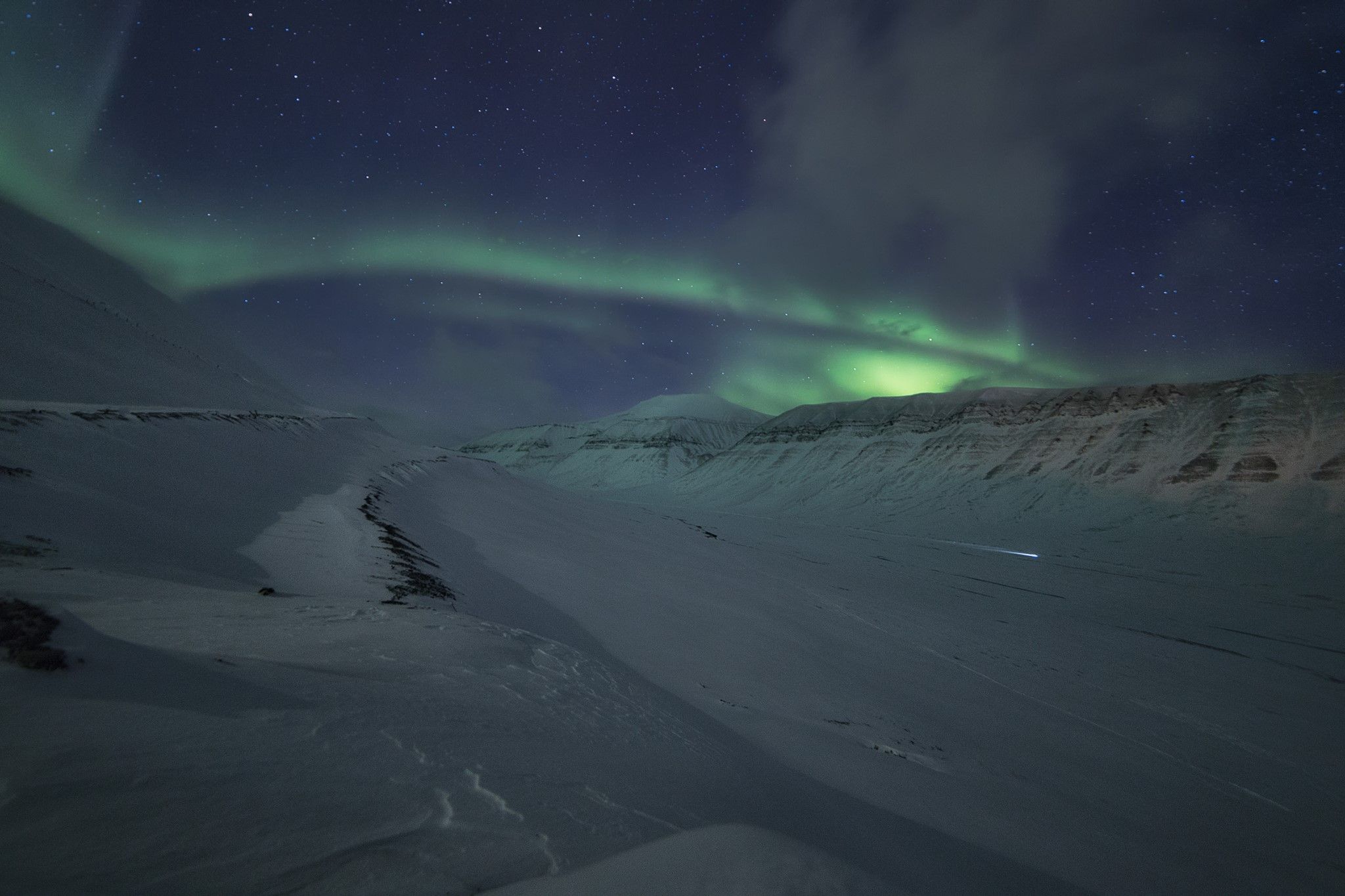 Snow-covered mountains and valley, with northern lights in the sky above.