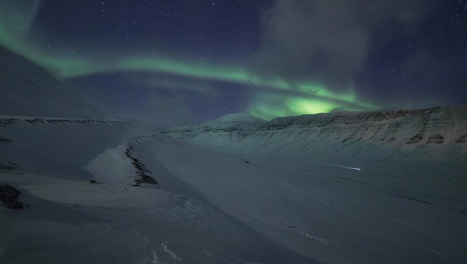 Snow-covered mountains and valley, with northern lights in the sky above.