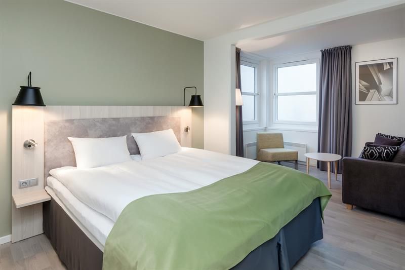 Moderne hotellrom med dobbeltseng, nattbord og dempet belysning.