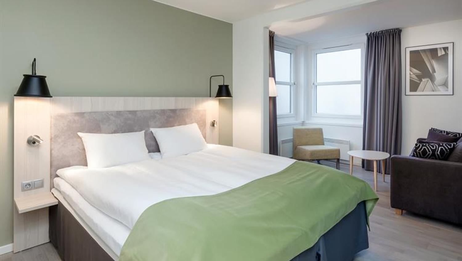 Moderne hotellrom med dobbeltseng, nattbord og dempet belysning.