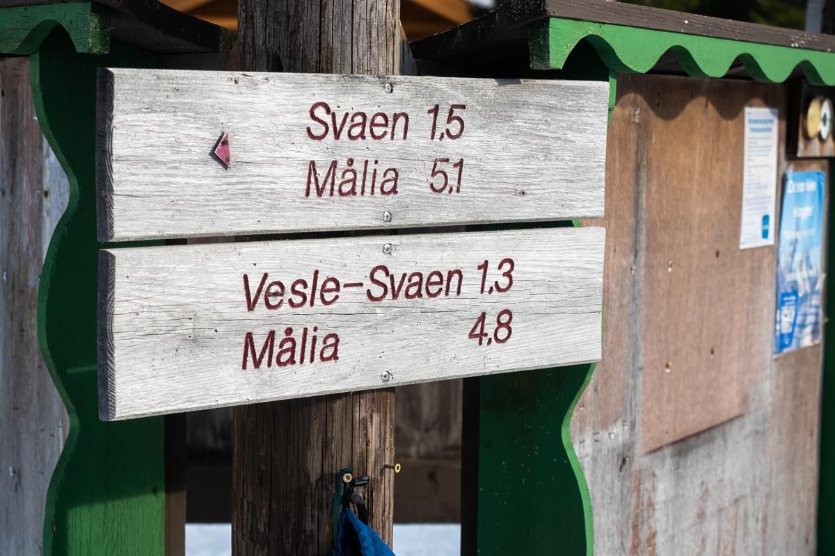 Et treskilt i et vinterområde som viser avstander til ulike turmål, montert på en liten bygning.