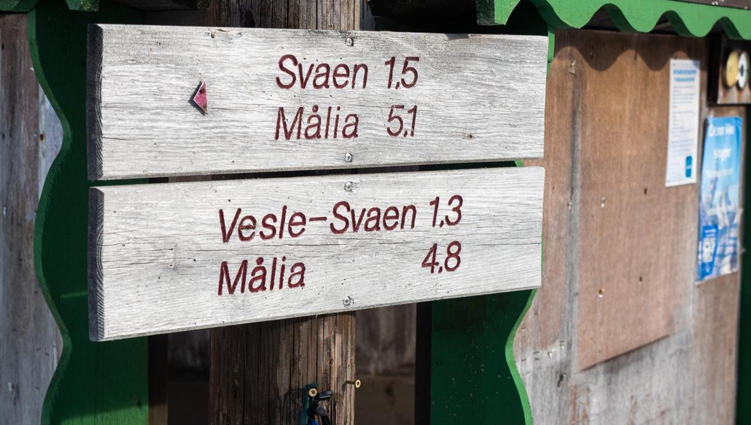 Et treskilt i et vinterområde som viser avstander til ulike turmål, montert på en liten bygning.