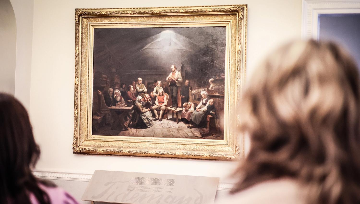 Et par ser på det store maleriet «Haugianerne» på Mandal museum, der Adolph Tidemand skildrer lekpredikanten Hans Nielsen Hauges følgere.