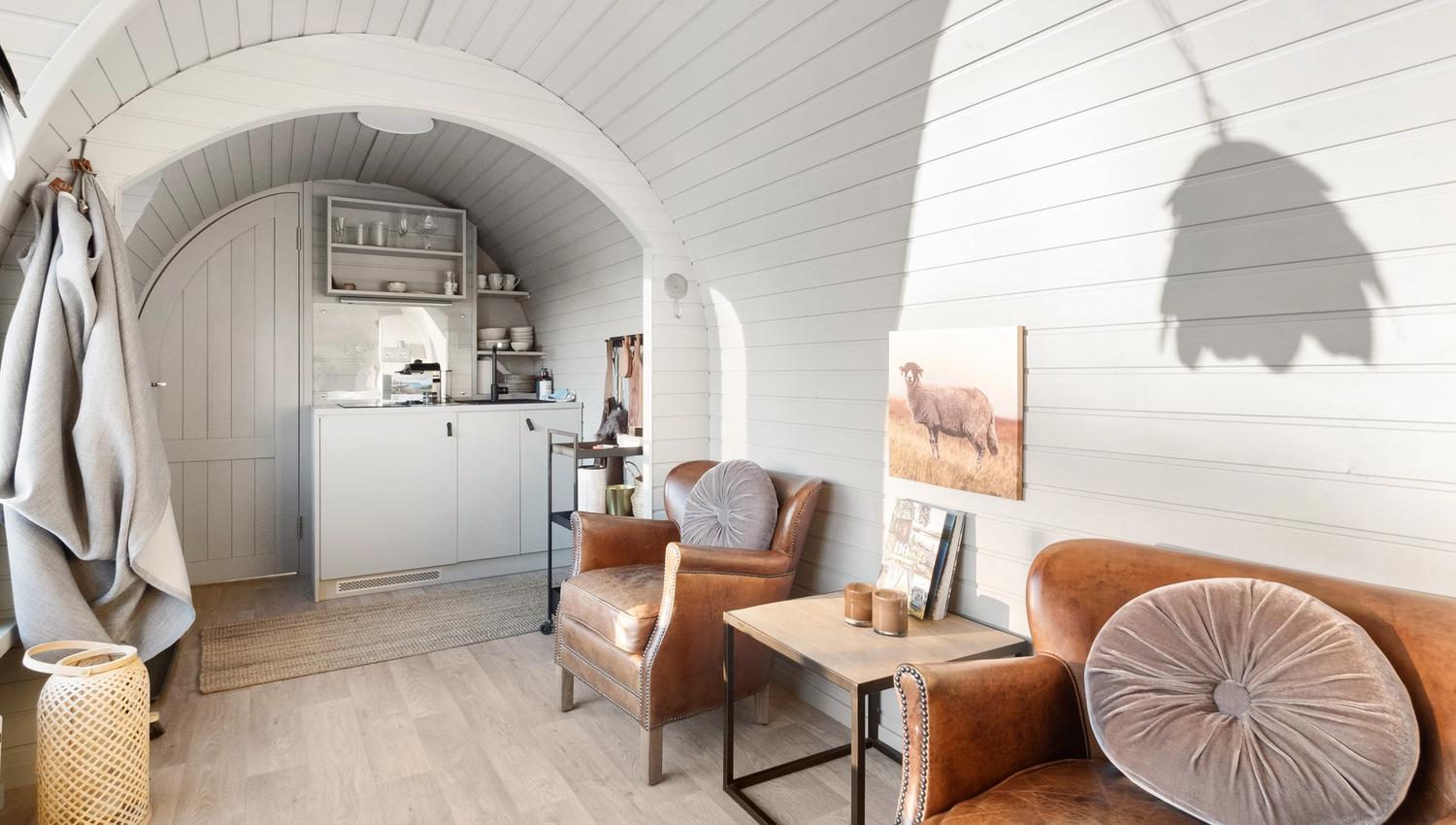 interiørbilde fra en hytte med hvite vegger, stoler og et lite kjøkken