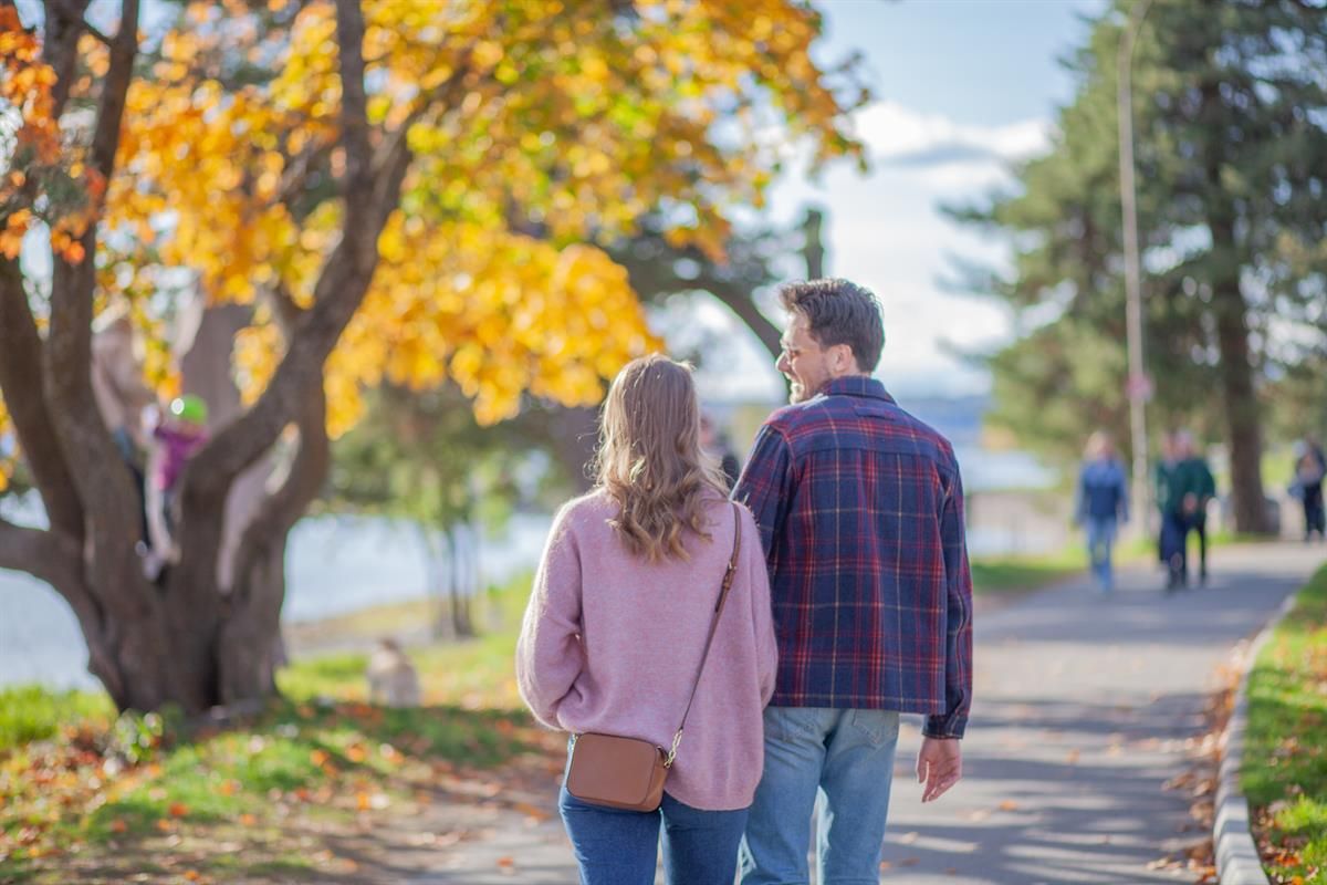 To personer går på en sti omgitt av trær med høstfarger.