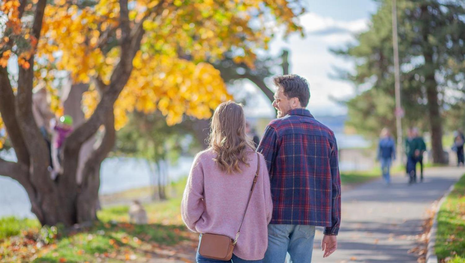 To personer går på en sti omgitt av trær med høstfarger.