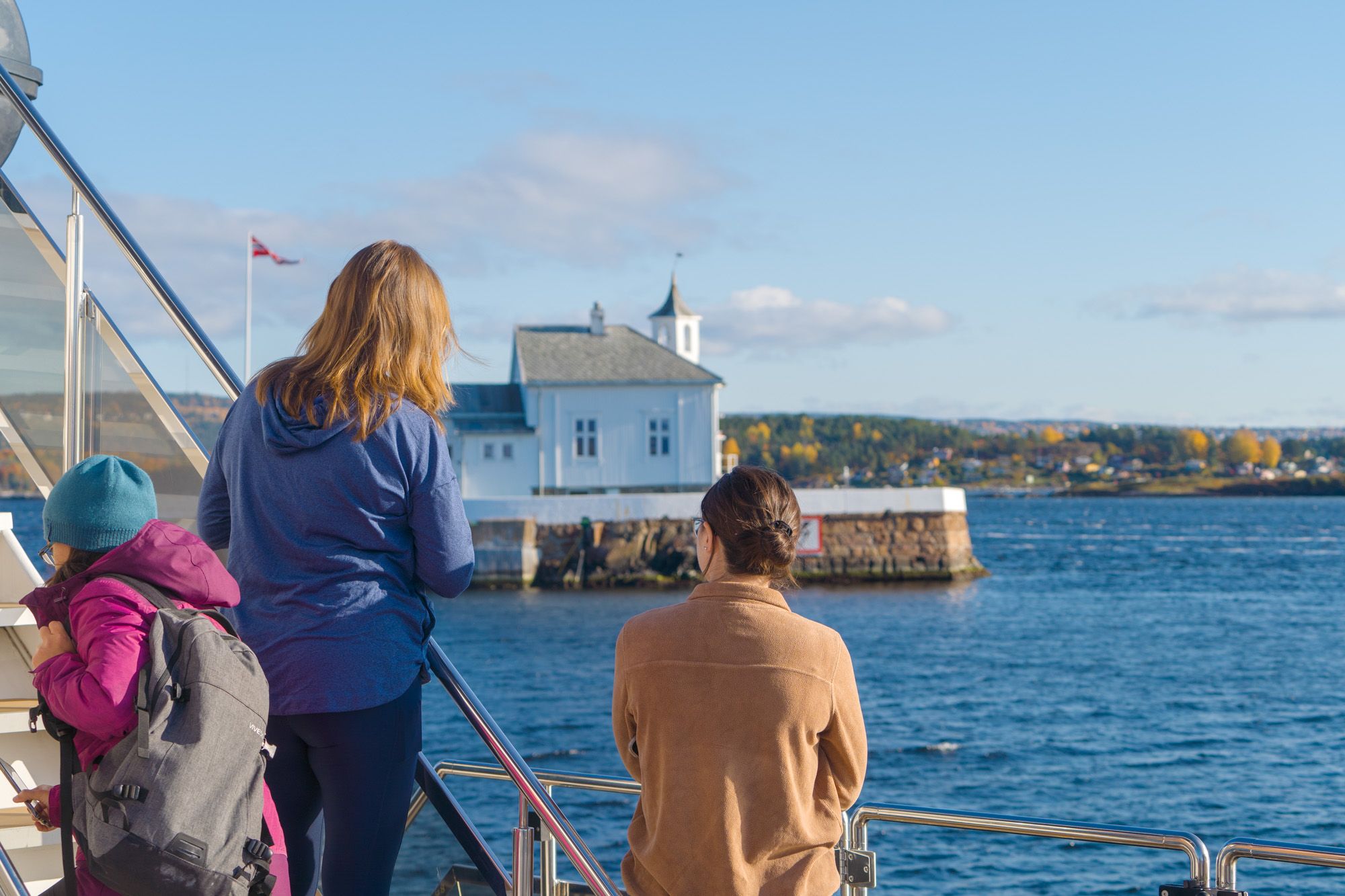People looking at a lighthouse in the fjord from the boat