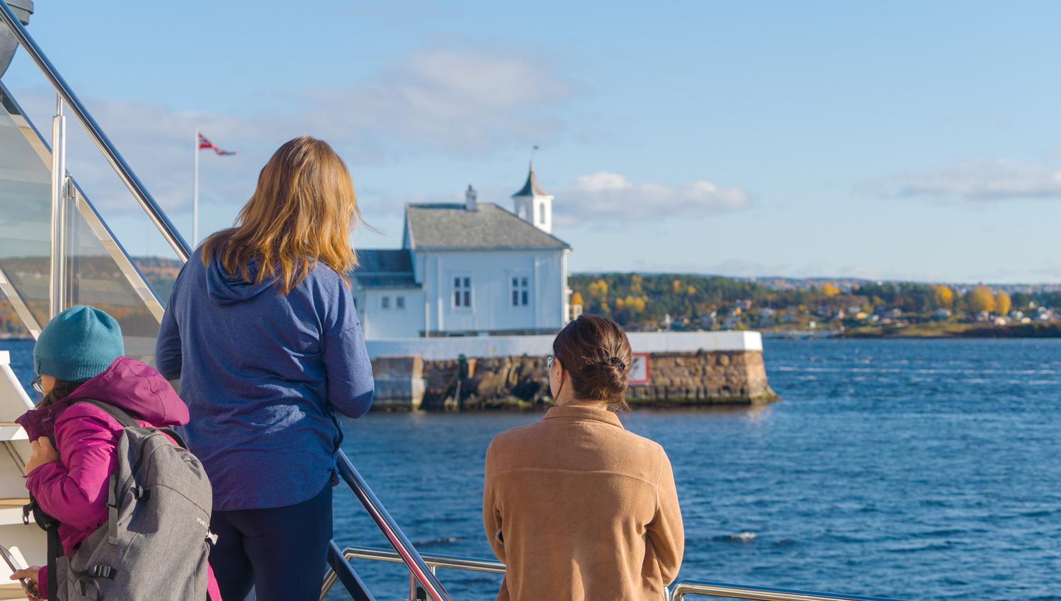 People looking at a lighthouse in the fjord from the boat