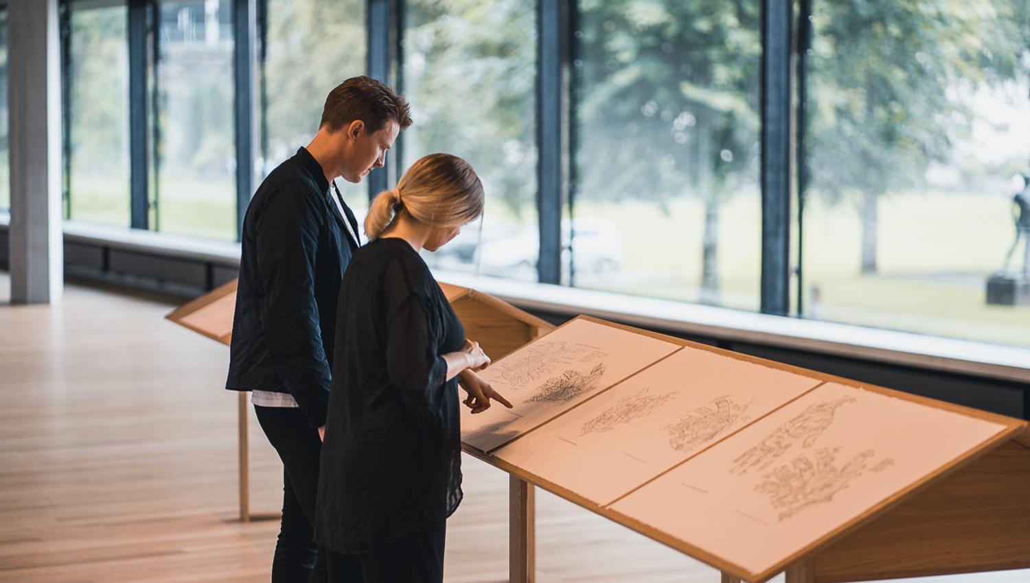 Besøkande studerar utstillingsmateriale i Kunsthuset Kabuso, med store vindauge ut mot naturen.