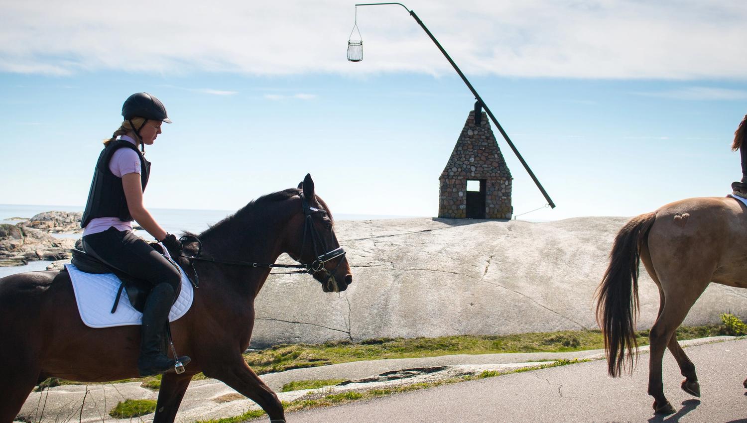 Horses and riders ride past the tilting lighthouse at the End of the World