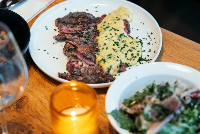 Juicy steak with béarnaise sauce and fresh salad served on a rustic wooden table.