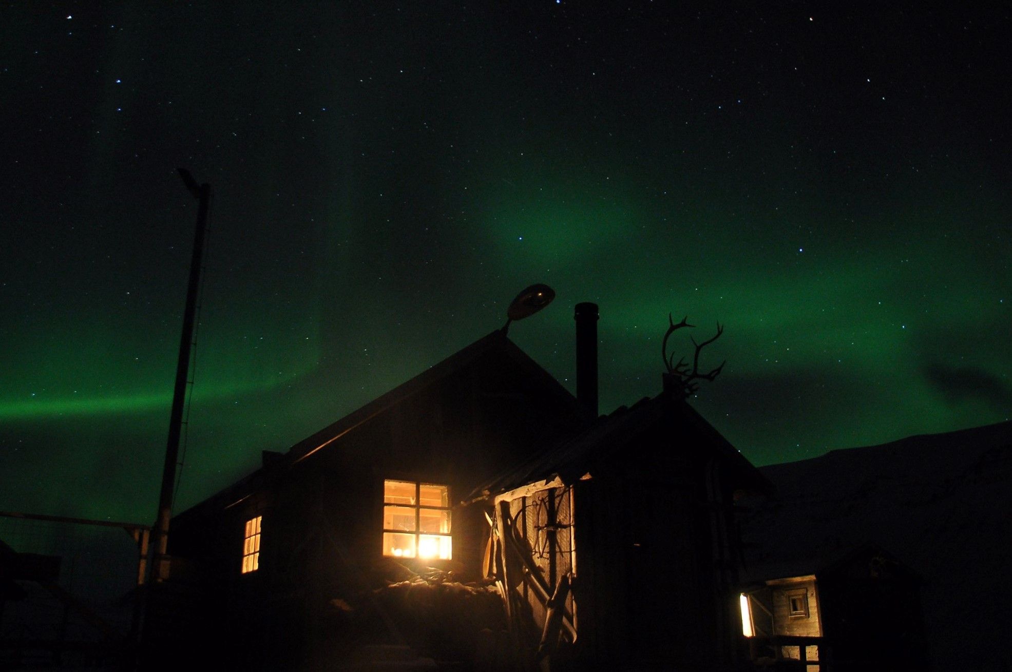 Cabin with light through the windows under the Northern Lights sky.