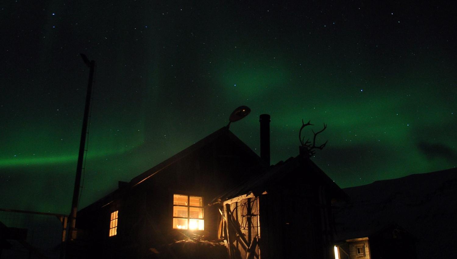 Cabin with light through the windows under the Northern Lights sky.