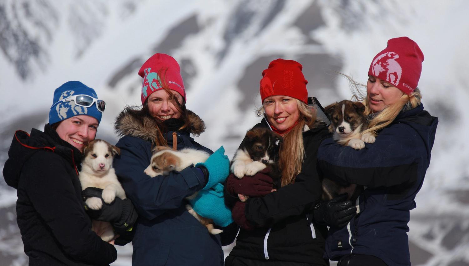 Fire personer poserer foran en fjellformasjon med en valp hver i armene.