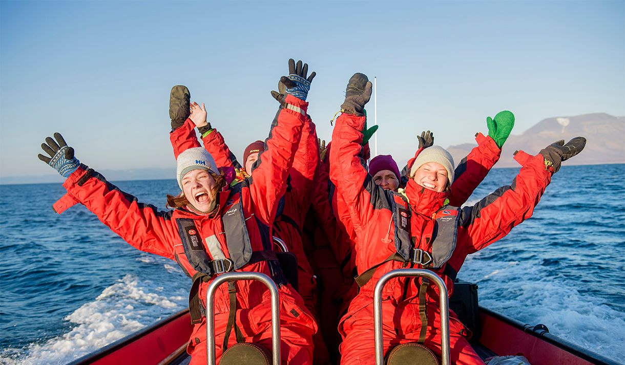 A group of guests sitting in a RIB boat at speed cheering with their arms outstretched