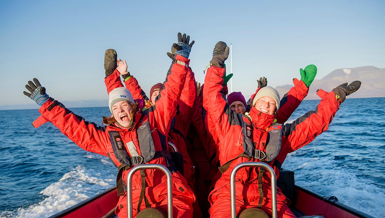 A group of guests sitting in a RIB boat at speed cheering with their arms outstretched