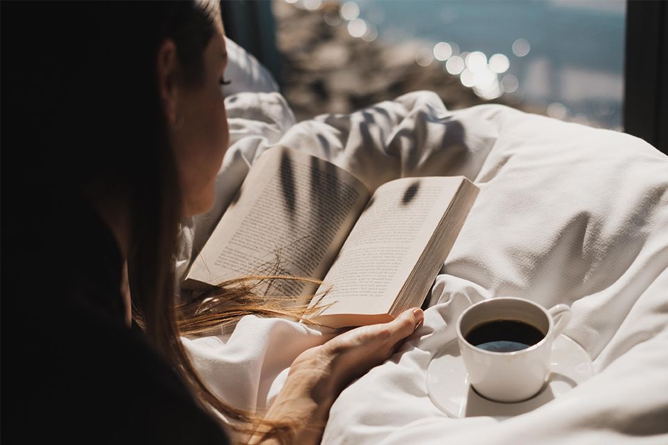 Dame leser bok i sollyset med en kaffekopp