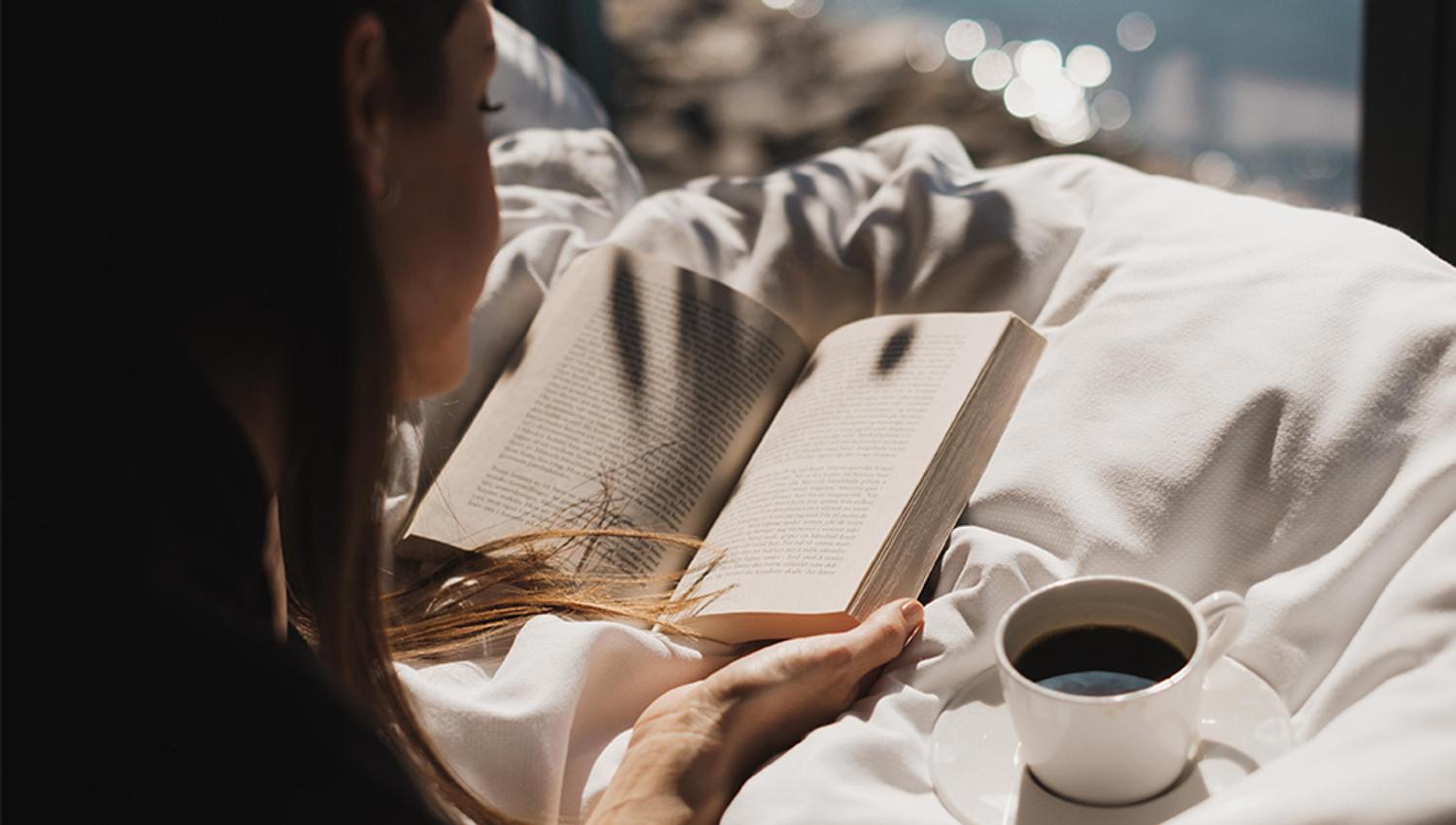 Dame leser bok i sollyset med en kaffekopp