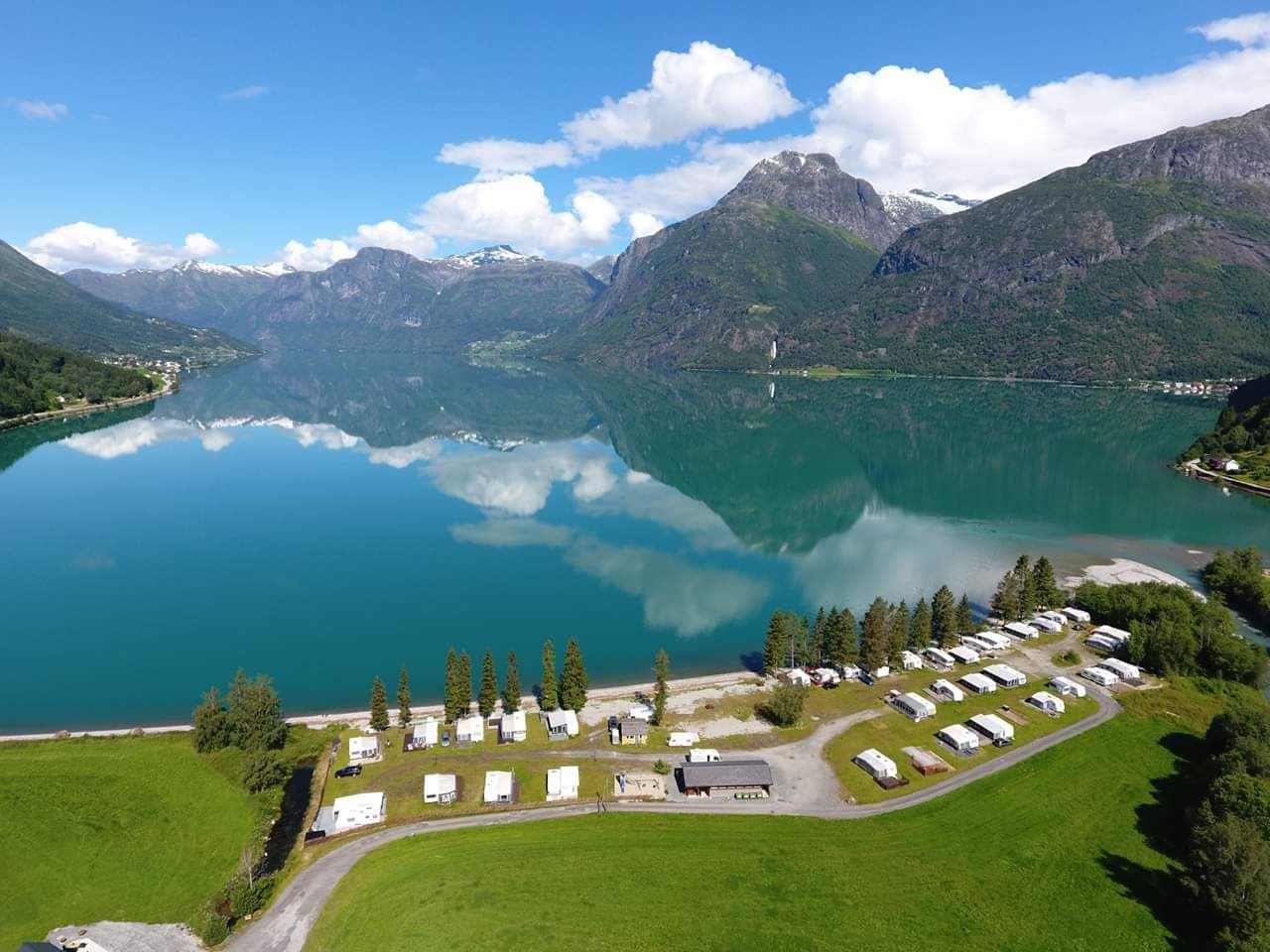 Droneutsikt over Grande Camping ved Oppstrynsvatnet i Oppstryn, omgitt av fjell og den blågrøne fargen frå brevatnet.