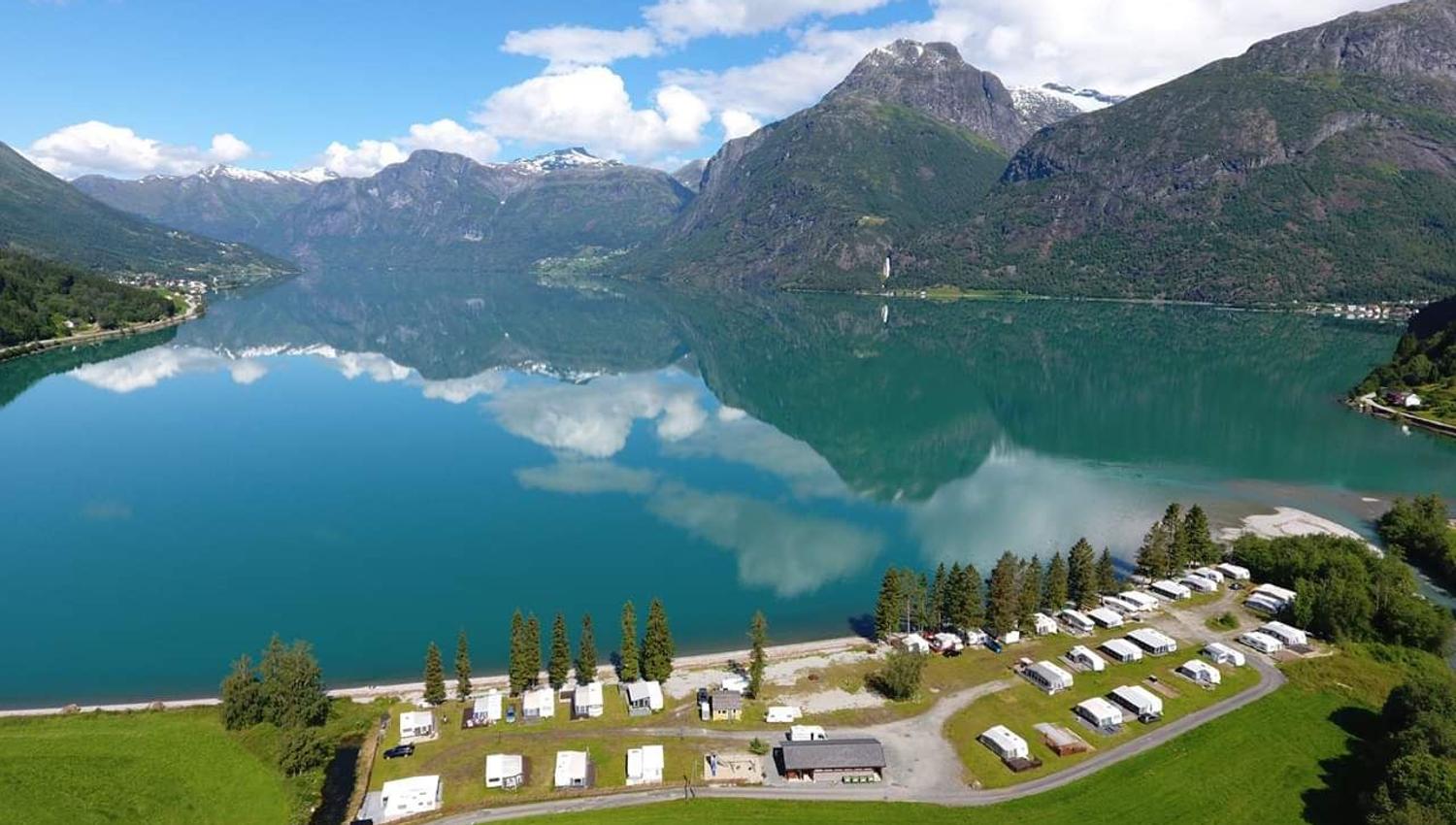 Droneutsikt over Grande Camping ved Oppstrynsvatnet i Oppstryn, omgitt av fjell og den blågrøne fargen frå brevatnet.