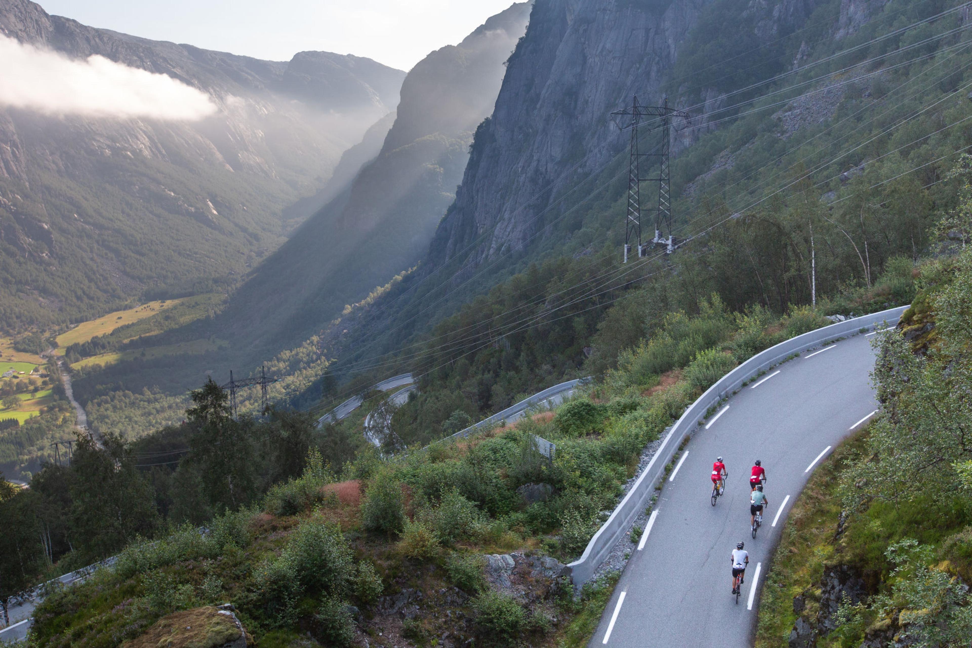 Norway Bike Experience. Tre syklister sykler opp en bakke med fjell og daler som utsikt
