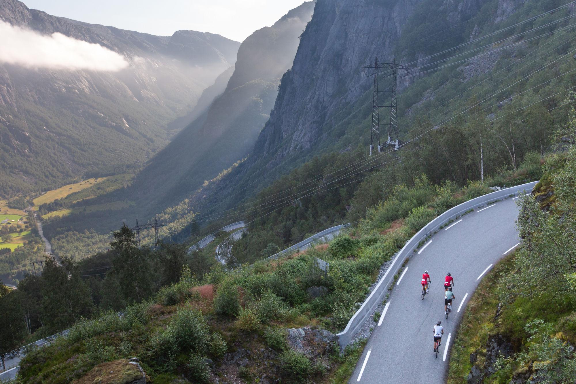 Norway Bike Experience. Tre syklister sykler opp en bakke med fjell og daler som utsikt